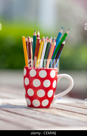 Färben färben Bleistifte in einem roten und weißen Polka Dot Becher draußen auf einem Holztisch Stockfoto