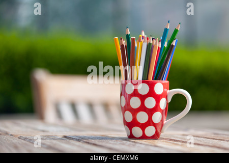 Färben färben Bleistifte in einem roten und weißen Polka Dot Becher draußen auf einem Holztisch Stockfoto