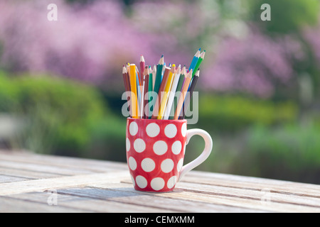 Färben färben Bleistifte in einem roten und weißen Polka Dot Becher draußen auf einem Holztisch Stockfoto