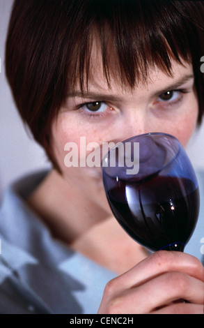 Nahaufnahme des weiblichen kurze brünette Haare Make-up subtilen blauen Hemd trinken Rotwein aus blauem Glas nach oben auf der Kamera Stockfoto