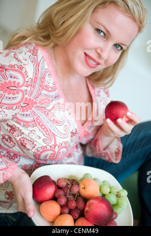 Nahaufnahme von größeren weiblichen langes blondes Haar, Jeans und rosa paisley V Neck Shirt hält Teller mit frischem Obst und einem Stockfoto