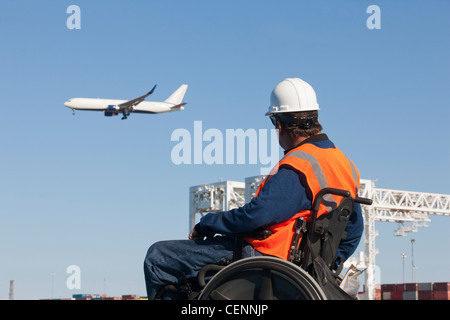 Transport-Ingenieur im Rollstuhl Flugzeug fliegen über Versandbehälter und Kräne im Hafen beobachten Stockfoto