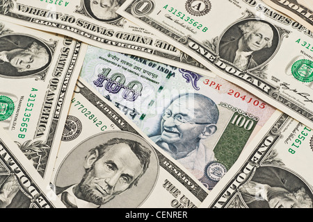 Viele US-Dollarnoten nebeneinander liegen. In der Mitte liegt eine Rechnung indischen 100 Rupien mit dem Porträt von Mahatma Gandhi. Stockfoto