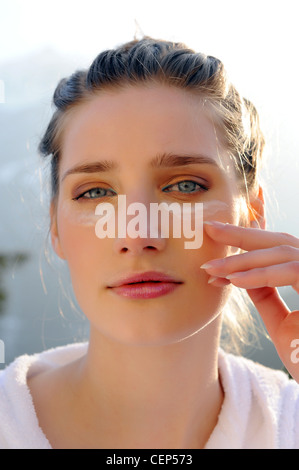 Frau trägt ein weißes Frottee-Gewand mit Augencreme unter ihren Augen Stockfoto