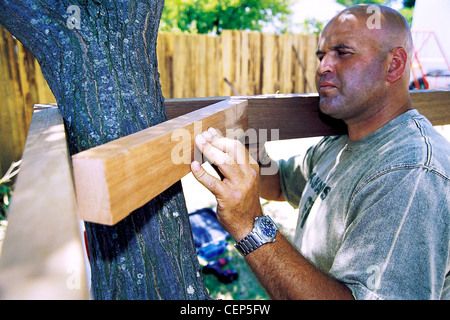 FORBuild ein Baumhaus Schritt männlichen anbringen der verstärkenden Holzbrett um den Baumstamm Stockfoto