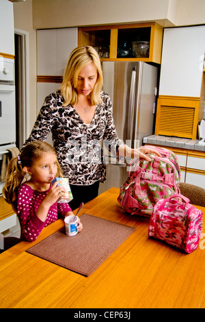 Eine 29 Jahre alte Mutter ruft ihre 6 jährige Tochter für die Schule fertig, wie sie ein gesundes Frühstück isst. MODEL-RELEASE Stockfoto