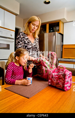 Eine 29 Jahre alte Mutter ruft ihre 6 jährige Tochter für die Schule fertig, wie sie ein gesundes Frühstück isst. MODEL-RELEASE Stockfoto