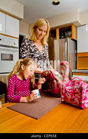 Eine 29 Jahre alte Mutter ruft ihre 6 jährige Tochter für die Schule fertig, wie sie ein gesundes Frühstück isst. MODEL-RELEASE Stockfoto