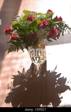 Sonnenschein am Strauß roter Rosen und Gypsophyla in Glasvase Stockfoto