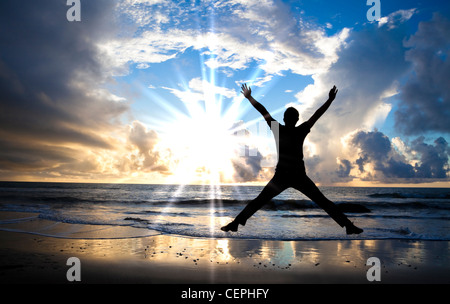 glücklicher Mann am Strand mit wunderschönen Sonnenaufgang springen Stockfoto