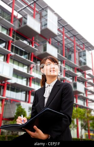 junge schöne Geschäftsfrau sitzen vor dem modernen Gebäude Stockfoto