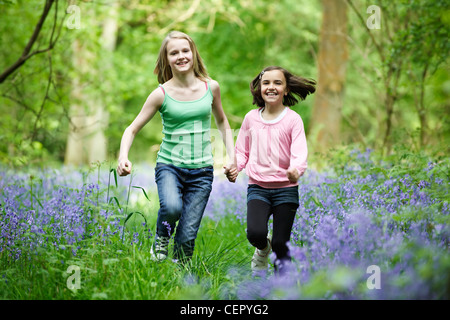 Zwei junge Mädchen laufen hand in hand durch ein Holz voller Glockenblumen. Stockfoto