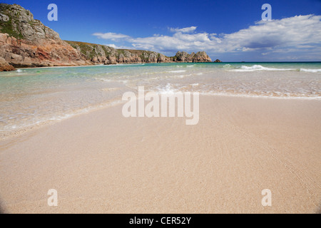 Ebbe am sandigen Strand von Porthcurno mit Logan Rock in der Ferne. Stockfoto