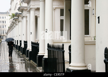 Ein Mann mit einem Regenschirm geht auf einer nassen Straße mit traditionellen Londoner Häusern gesäumt. Stockfoto