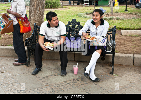 junge & Mädchen-technical High School Schüler in Schuluniform Mittagessen auf einer viktorianischen Schmiedeeisen Bank in Llano Park Oaxaca Stockfoto