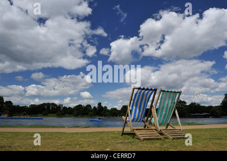 Zwei Liegestühle durch die Serpentinen im Hyde Park an einem luftigen, sonnigen Tag. Stockfoto