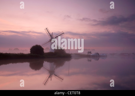 Eine neblige Sicht über das Wasser zu Thurne Mill bei Sonnenaufgang. Stockfoto