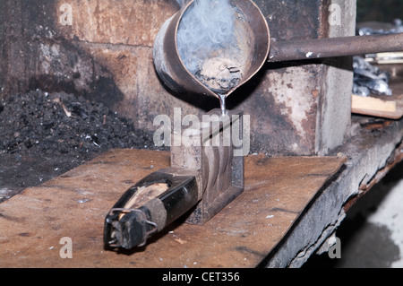 Schmelzendes Blei, um selbstgemachte Sinker zum Angeln herzustellen. Geschmolzenes Metall wird aus einer Pfanne in eine quadratische Gussform in einer Metallwerkstatt gegossen. Stockfoto