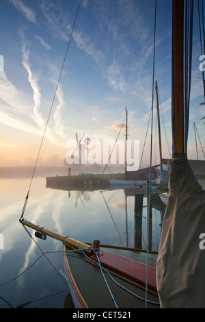 Blick über den Bug eines Segelschiffes auf dem Fluß Thurne durch Dawn Nebel in Richtung Thurne Entwässerung Mühle auf den Norfolk Broads. Stockfoto