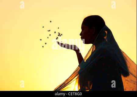 Indische Mädchen trägt einen Sternen Schal Sterne in die Luft bläst. Silhouette Stockfoto