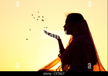 Indische Mädchen trägt einen Sternen Schal Sterne in die Luft bläst. Silhouette Stockfoto