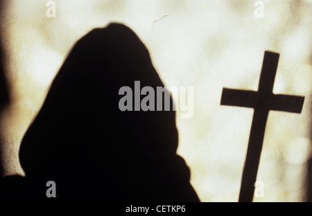 Vermummten Mönch hält große Kruzifix und Silhouette gegen helle weiße Wand Stockfoto