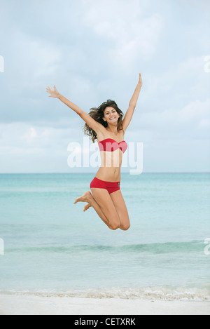 Junge Frau im Bikini springen in der Luft am Strand Stockfoto