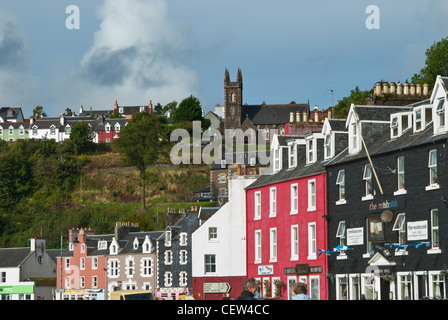 Parade der bunten Häuser im Vordergrund mit Hügel hinter mit einer Kirche in Tobermory auf der Isle of Mull Stockfoto