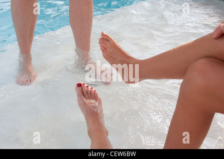 Beine und Füße in und in der Nähe von Schwimmbadwasser.  Drei Menschen genießen den Pool. Stockfoto