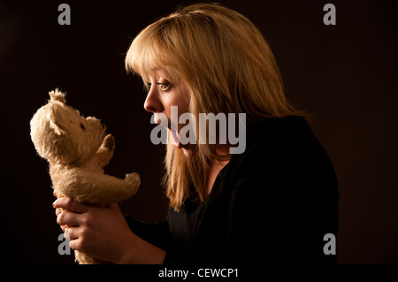 eine blonde behaarte Teenager Frau zieht ein Gesicht und spielt mit ihren alten ramponierten Teddybär Stockfoto