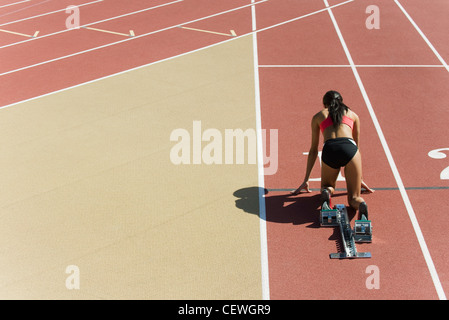 Frau kauerte in Startposition auf Laufstrecke, Rückansicht Stockfoto