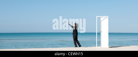 Geschäftsmann am Strand mit Blick auf den Ozean mit Arme angehoben, hintere Ansicht Stockfoto