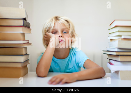 Junge sitzt zwischen zwei Stapel von Büchern mit gelangweilten Gesichtsausdruck Stockfoto