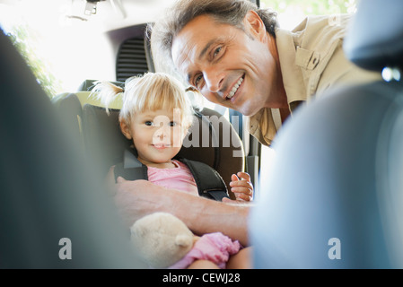 Vater, kleines Mädchen in Autositz befestigen, Lächeln beide in die Kamera Stockfoto