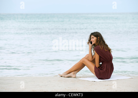Junge Frau sitzt am Strand, mit Handy Stockfoto