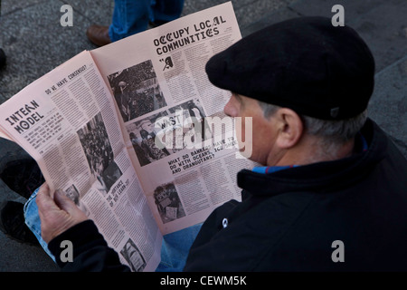 Ein Mann sitzt eine Kopie des besetzten Times of London an der London OLSX besetzen Protest zu lesen. Stockfoto