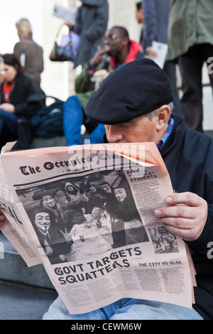 Ein Mann sitzt eine Kopie des besetzten Times of London an der London OLSX besetzen Protest zu lesen. Stockfoto