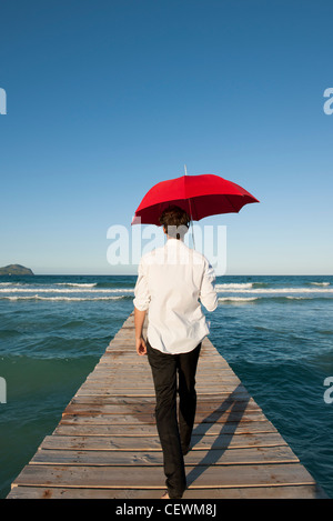 Mann zu Fuß auf Pier mit roten Regenschirm, Rückansicht Stockfoto