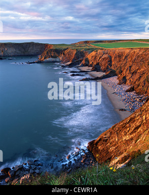 Die weichen Felsen und Felsbrocken übersäten Strand von Traeth Llyfn Bucht sind ein reichhaltiges warmes Gold von der untergehenden Sonne gemalt. Stockfoto