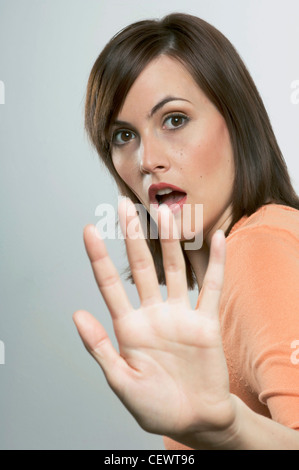 Weibliche Schulter Länge gerade brünette Haare, tragen orange Jumper, braune Augen Make-up, roter Lippenstift, Mund offen, Hand Stockfoto