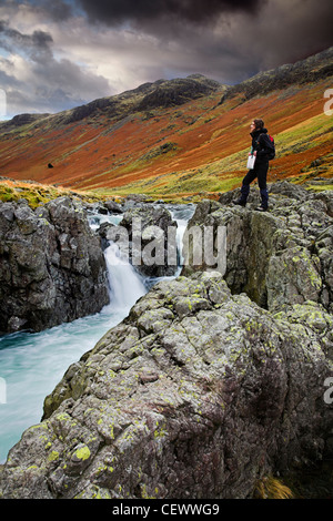 Junge Frau, die auf Felsen neben dem Fluß ESK Der Fluß Esk beginnt im großen Moos unter Scafell Pike in der englischen Lak Stockfoto