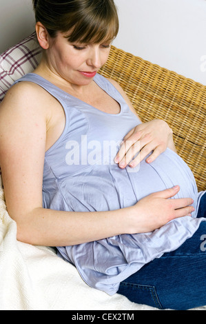 Trächtige Weibchen auf Wicker Sofa liegend mit Hände ruhen auf Stoß Stockfoto