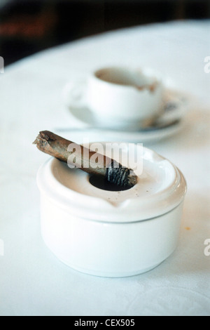 Andalusische Essen halben geräucherten Zigarre ruht auf einem weißen Aschenbecher mit einem Milchkaffee Tasse und Untertasse im Hintergrund Stockfoto