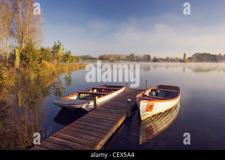 Zwei Ruderboote gebunden auf einem Holzsteg auf Stockente See an der Wiltshire Wildlife Trust des neuen niedrigeren Moor Farm Naturschutzgebiet. Stockfoto