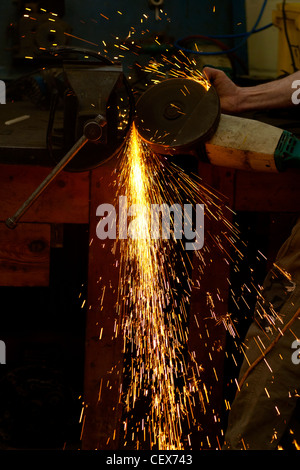 Arbeiten Schmied Verfeinerung ein Stück Metall durch Schleifen, um die Oberfläche zu glätten.  Funken fliegen von der Reibung. Stockfoto