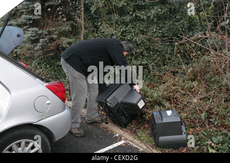 Ein Mann illegal dumping (Fly tipping) einige große Gegenstände, einschließlich Fernsehern auf der Seite ein Parkplatz zur Verfügung. (Gestellt). Stockfoto