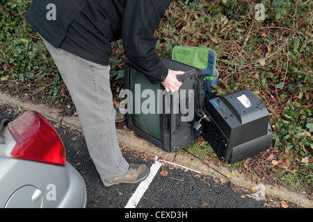 Ein Mann illegal dumping (Fly tipping) einige große Gegenstände, einschließlich Fernsehern auf der Seite ein Parkplatz zur Verfügung. (Gestellt). Stockfoto