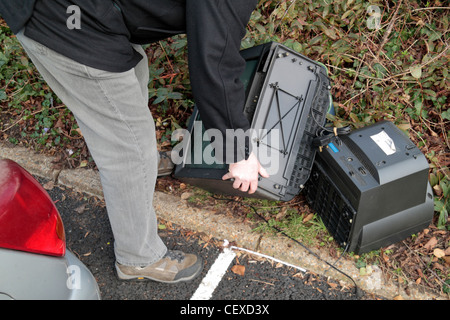 Ein Mann illegal dumping (Fly tipping) einige große Gegenstände, einschließlich Fernsehern auf der Seite ein Parkplatz zur Verfügung. (Gestellt). Stockfoto
