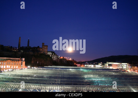 Blick über Edinburgh Waverley Station von North Bridge Skyline Calton Hill mit großen Mond im dunklen blauen Nachthimmel. Stockfoto