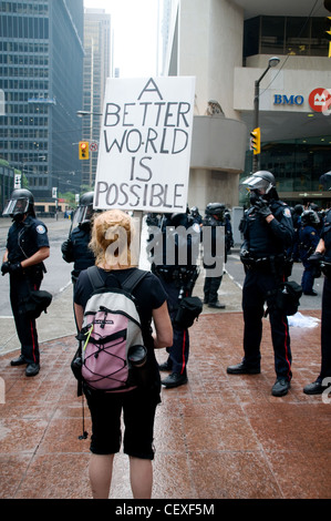 Eine junge weibliche Demonstrant hält ein Schild vor Toronto Bereitschaftspolizei während der G20-Gipfel in Toronto, Ontario, Kanada, im Sommer 2010. Stockfoto